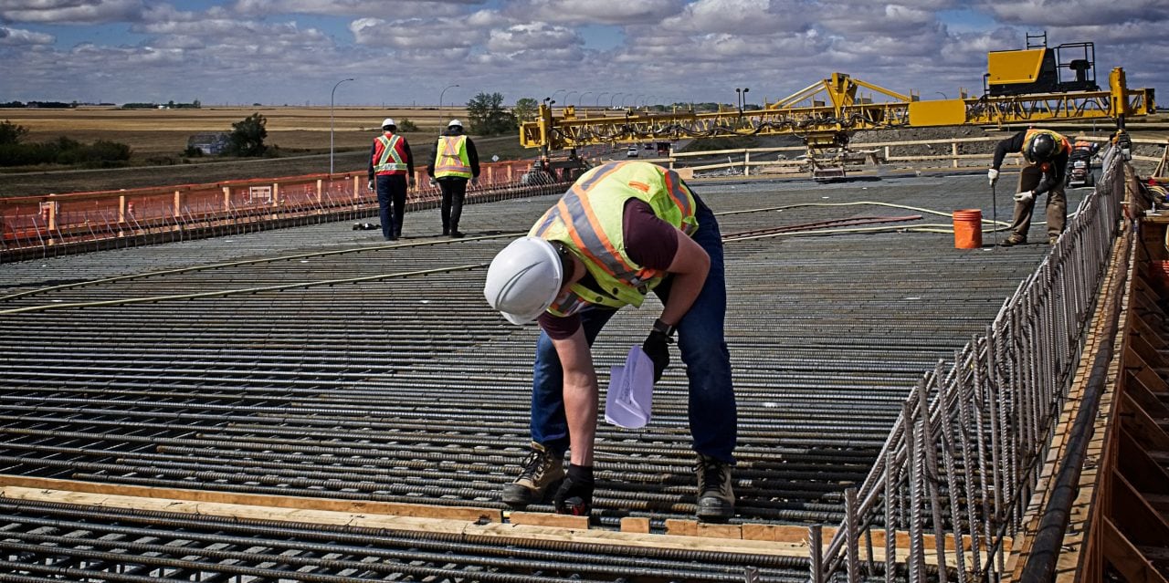 A bridge engineer inspecting spacing diameter and height of steel reinforcing bars with a tape measure on the bridge deck prior to pouring concrete on the reinforced deck supported by steel girders