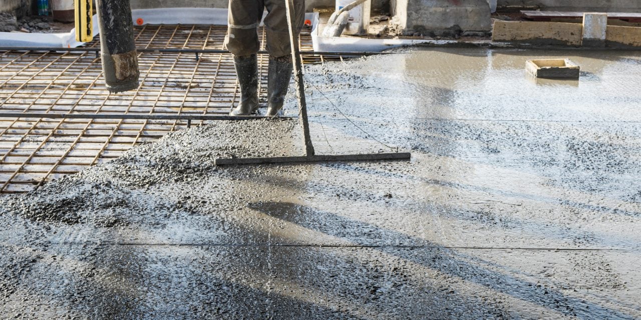 Construction worker leveling a poured concrete floor in an industrial workshop. Legs in boots in concrete. Surface concreting. Monolithic reinforced concrete works